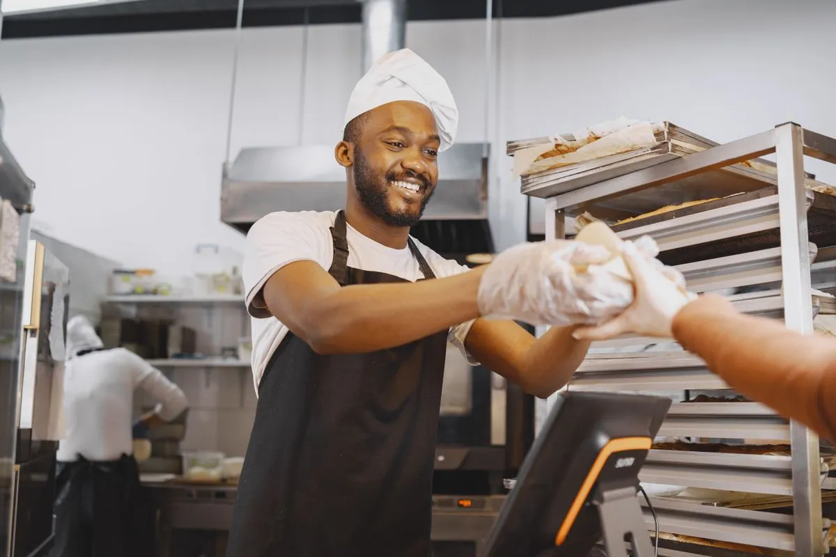 Een lachende bakker geeft een klant vers brood aan over de toonbank